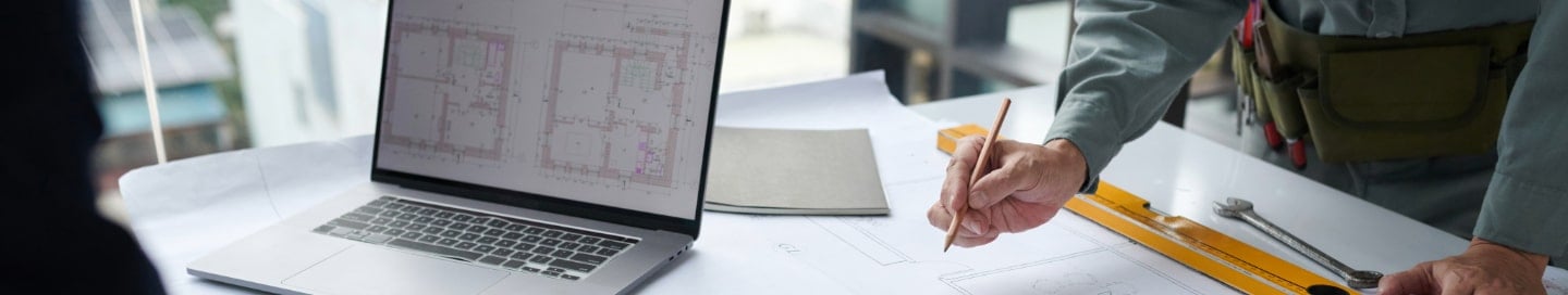 A building designer working with blueprints and a laptop. A building designer working with blueprints and a laptop.